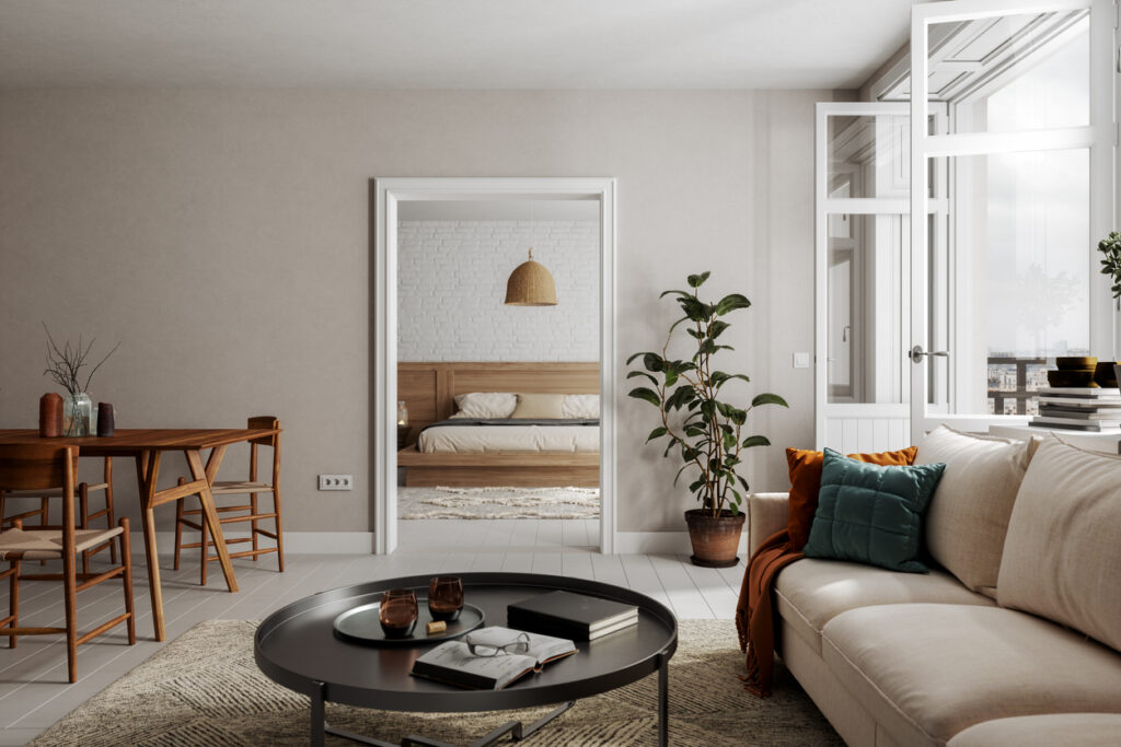 Interior de un moderno apartamento mostrando un salón con sofá beige, mesa redonda negra y ventanas grandes, iluminado naturalmente.